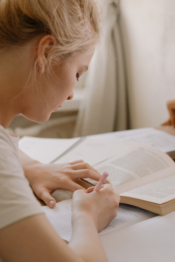 dziewczyna pochylona nad książkami i trzymająca w dłoni długopis
